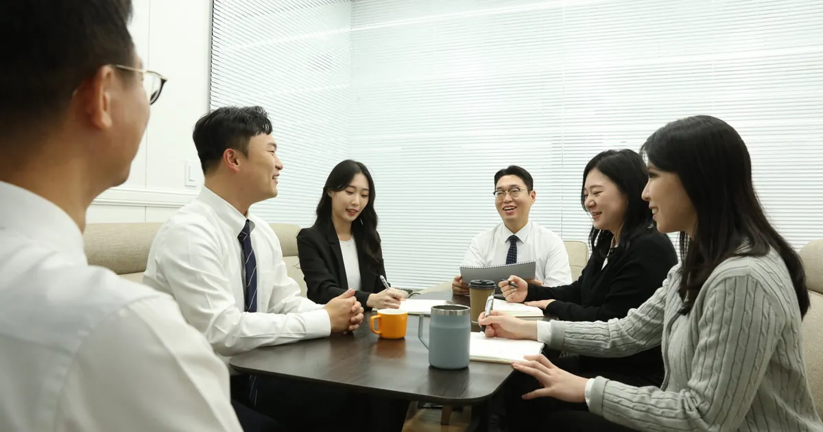 회의실 소파에 여섯 사람이 탁자를 가운데 두고 둘러앉아 수첩과 컵을 놓고 이야기하고 있다
