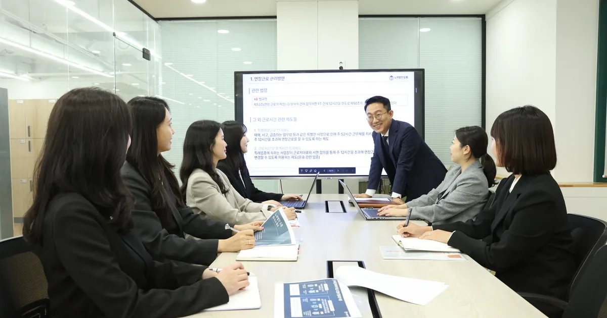 회의실에서 정장을 입은 사람들이 화면을 앞에 두고 탁자에 둘러앉아 이야기하고 있다