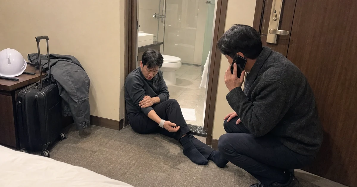 출장 숙소 욕실 문턱에서 다친 근로자의 상태를 확인하며 동료가 도움을 요청하는 모습